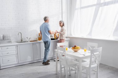 Mutfakta yemek yaparken el ele tutuşan gülümseyen olgun bir çift.