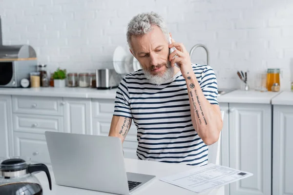 Tätowierter Älterer Mann Telefoniert Der Nähe Von Rechnungen Und Laptop — Stockfoto