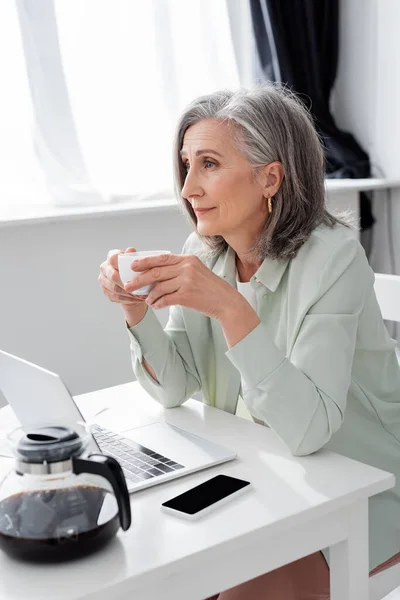 Freelancer Meia Idade Segurando Copo Perto Gadgets Casa — Fotografia de Stock