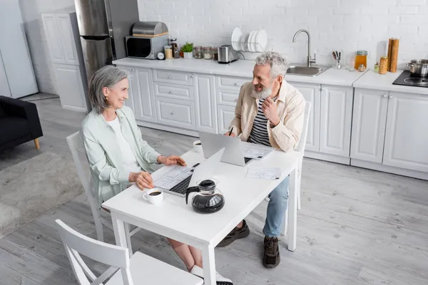 Cheerful Mature Couple Looking Each Other Bills Coffee Laptops Home — Stock Photo, Image
