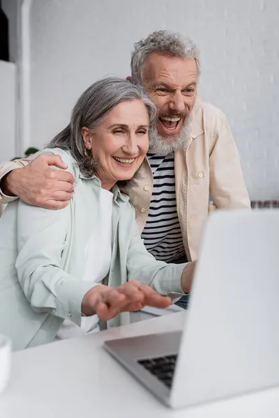 Eccitato Uomo Abbracciare Moglie Matura Vicino Computer Portatile Offuscata Casa — Foto Stock