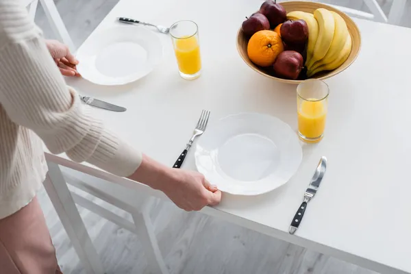 オレンジジュースや果物の近くのテーブルの上に皿を置く女性の作物ビューキッチンで — ストック写真