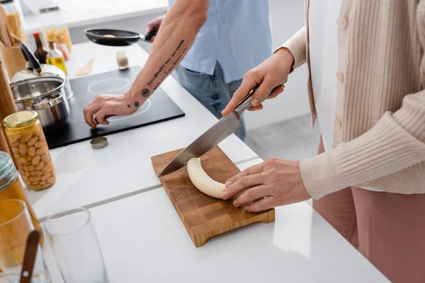 Cropped View Woman Cutting Banana Blurred Husband Frying Pan Kitchen — Stock Photo, Image