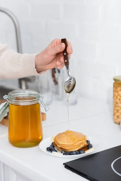 台所で果物とパンケーキに蜂蜜を注ぐ女性の作物ビュー — ストック写真
