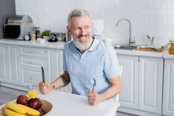 Mutfakta Portakal Suyu Meyvelerin Yanında Çatal Bıçak Taşıyan Gülümseyen Olgun — Stok fotoğraf
