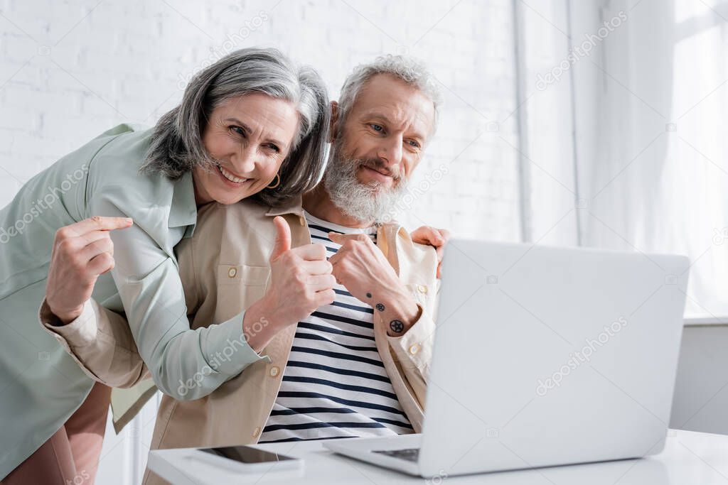 Smiling mature couple gesturing during video call on laptop in kitchen 