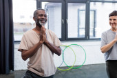 Lächelnder afrikanisch-amerikanischer Mann praktiziert Yoga in der Nähe eines älteren Freundes im Sportzentrum 