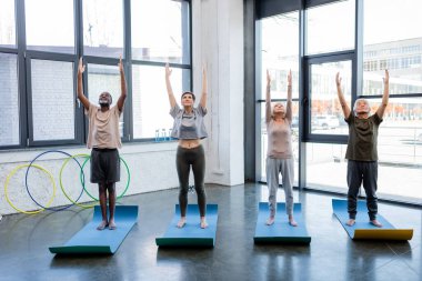 Dağda yoga yapan çok kültürlü son sınıf öğrencileri spor merkezindeki spor paspasları üzerinde poz veriyorlar. 