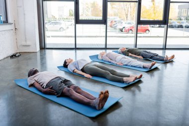 Spor merkezinde yoga minderlerinin üzerinde yatan ırklar arası yaşlılar. 