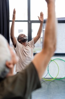 Gülümseyen Afrikalı Amerikalı adam yoga pozisyonunda spor merkezinde duruyor. 