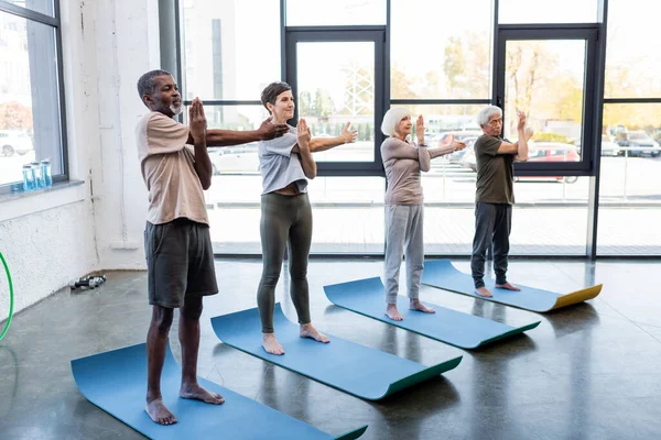 不同种族的老年人在体育馆的床垫上练习瑜伽 — 图库照片