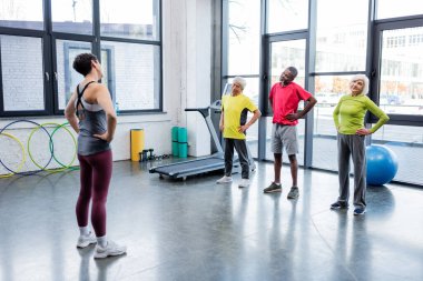 Spor salonunda antrenör yakınında egzersiz yapan çok ırklı yaşlı insanlar 