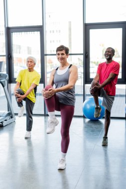 Spor salonunda çok ırklı insanların yanında çalışan gülen bir antrenör. 