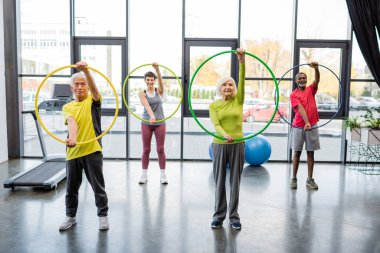 Çok ırklı insanlar spor salonunda hula hoopla antrenman yapıyor. 