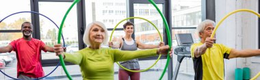 Smiling multicultural people exercising with hula hoops in gym, banner  clipart
