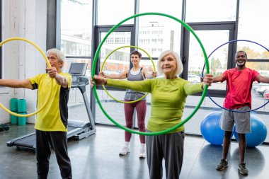 Interracial elderly people training with hula hoops in sports center  clipart