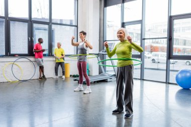 Mutlu yaşlı kadın hula hoop ile spor merkezinde egzersiz yapıyor. 