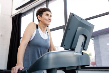 Gülümseyen sporcu kadın spor salonunda koşu bandında çalışıyor. 