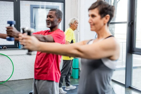 Elderly asian man training on treadmill near blurred interracial people in sports center