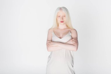 Albino elbiseli kadın kollarını çapraz açmış beyazlar içinde yalnız duruyor. 