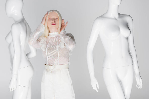 Stylish albino woman looking at camera near mannequins isolated on grey