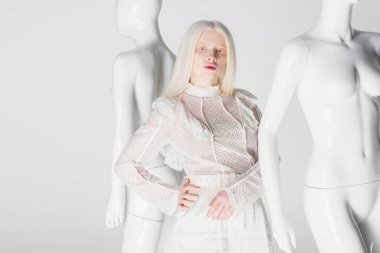Bluzlu genç albino kadın, beyaz tenli mankenlerin yanında el ele tutuşuyor. 
