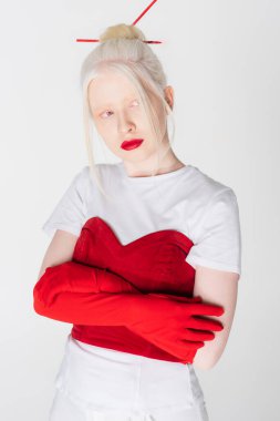 Pretty albino model in red gloves and hair sticks crossing arms isolated on white clipart