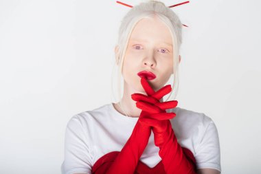 Kızıl saçlı ve eldivenli albino model beyaz kameraya bakıyor.