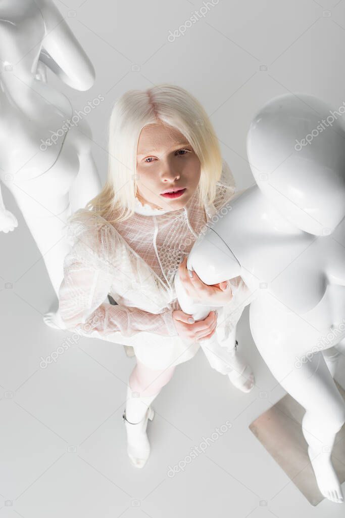 Overhead view of trendy albino woman in blouse standing near mannequin on white background 