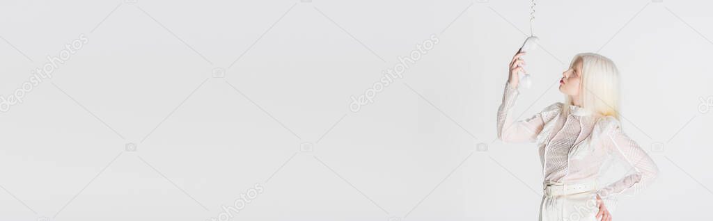 Side view of young albino model holding telephone handset isolated on white, banner 