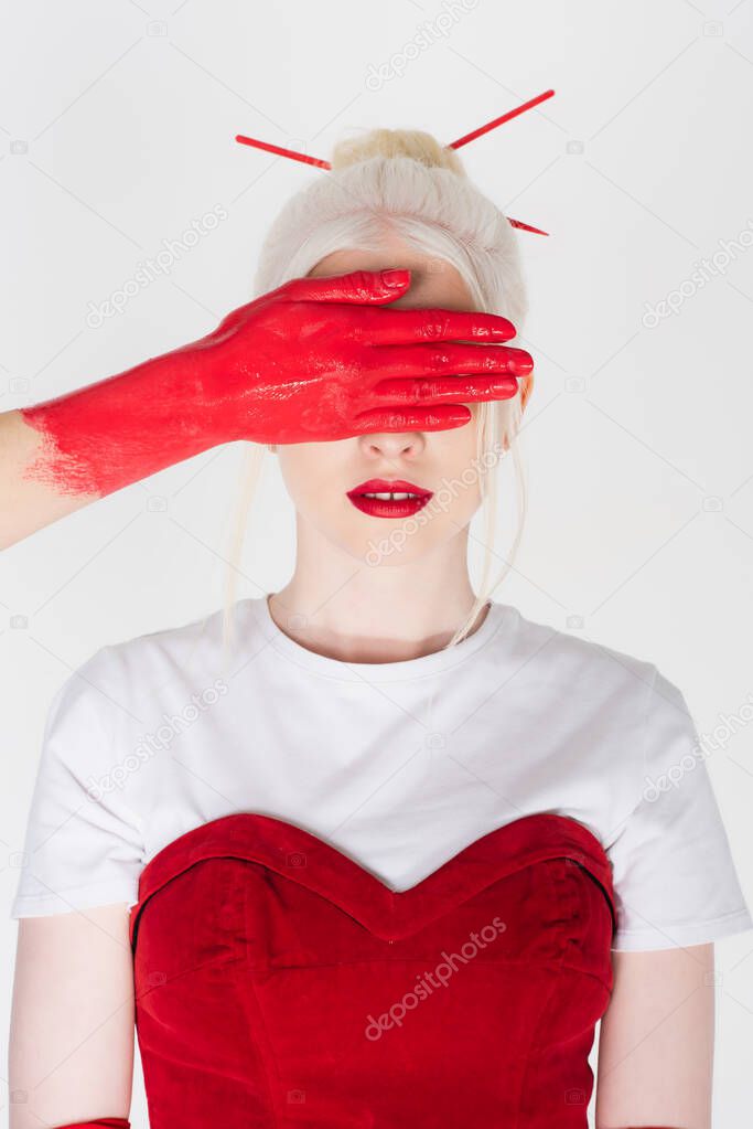 Woman with red paint on hand covering eyes of blonde model isolated on white
