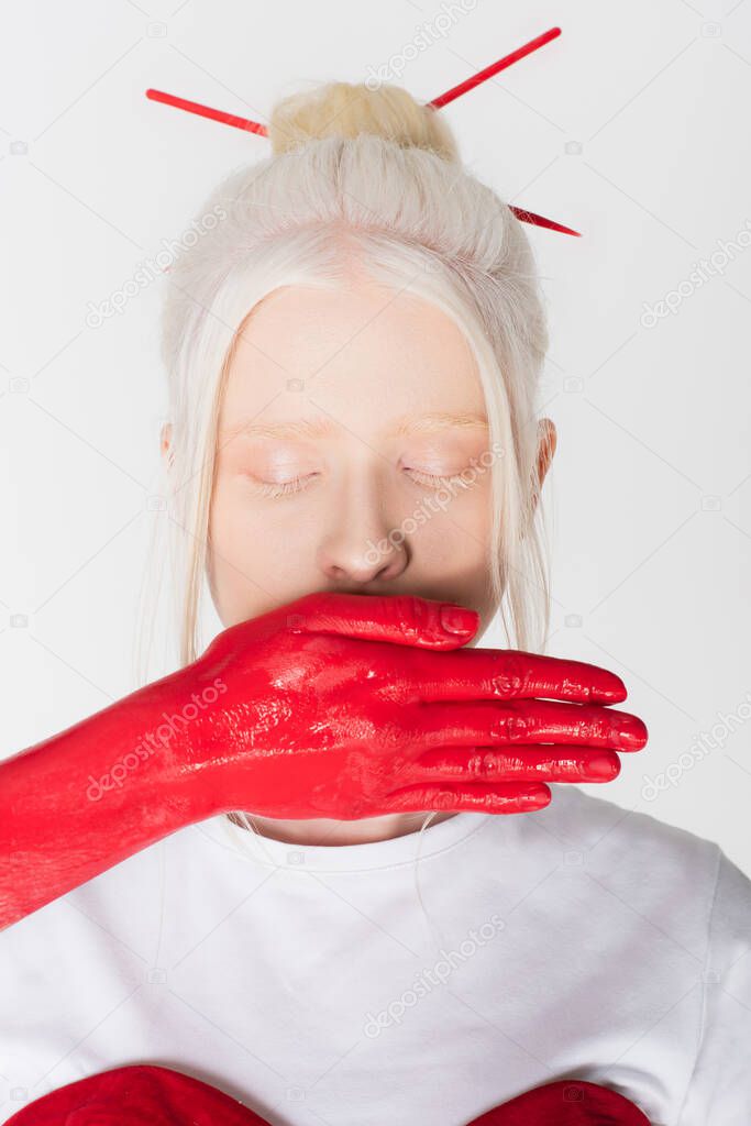 Woman with hand in red paint covering mouth of albino model isolated on white