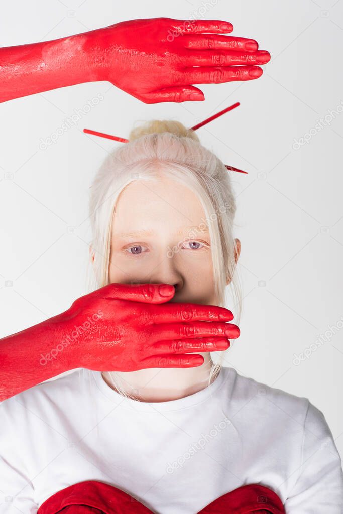 Female hands in red paint near stylish albino model isolated on white