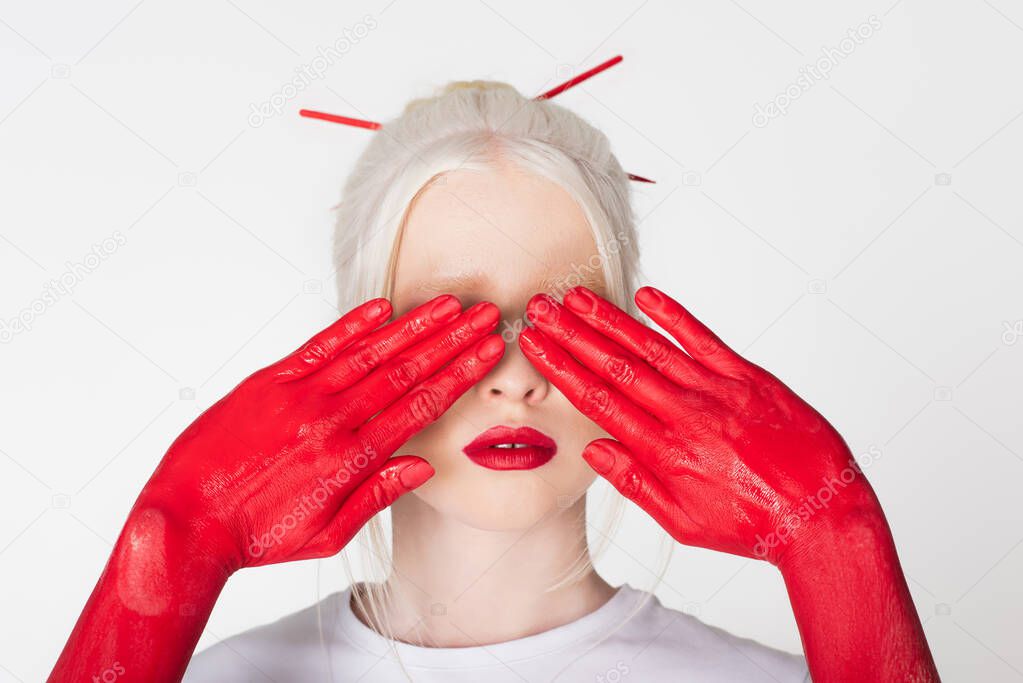 Female hands in paint covering eyes of albino model isolated on white
