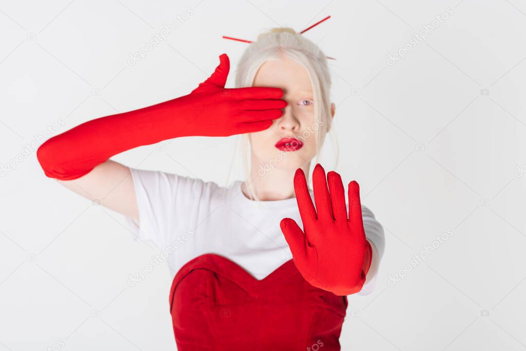 Blurred albino model in red gloves showing stop sign isolated on white
