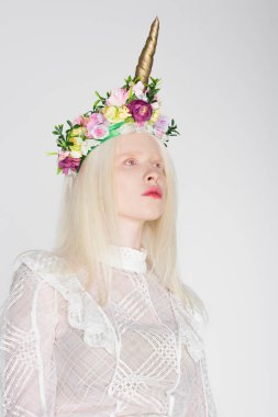 Bluz ve çiçek desenli albino manken beyaz bir çelenge bakıyor.