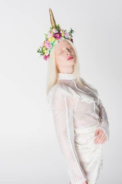 Genç albino kadın, bluz ve çelenk giymiş, çiçekli ve boynuzlu.