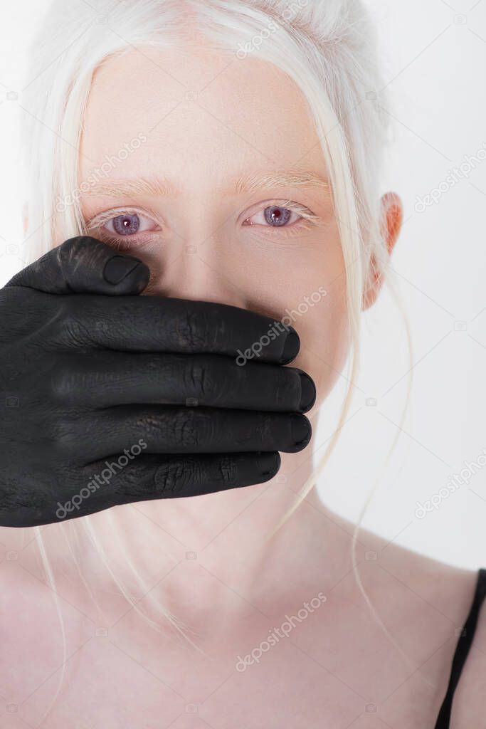 Male hand in black paint covering mouth of albino model isolated on white