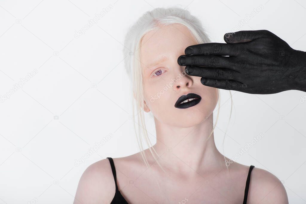 Male hand in black paint covering eye of albino woman isolated on white