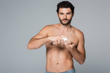 shirtless man applying toner on cotton pad and looking at camera isolated on grey clipart