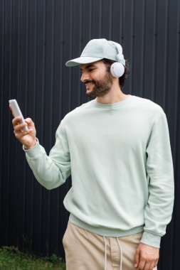 Kablosuz kulaklıklarla müzik dinleyen ve cep telefonunu metal çitlerin yanında tutan bir adam.