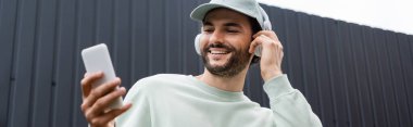Kablosuz kulaklıklarla müzik dinleyen ve tellerin yanında cep telefonu kullanan kapitalist bir adam.