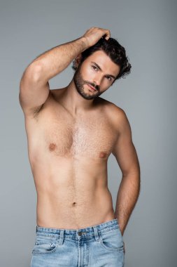 Dalgalı saçlı yakışıklı genç adam gri kameraya bakıyor.