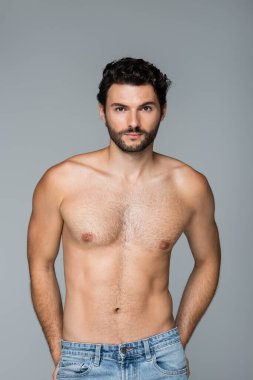 İyi görünümlü sakallı bir adam gri kameraya bakıyor.