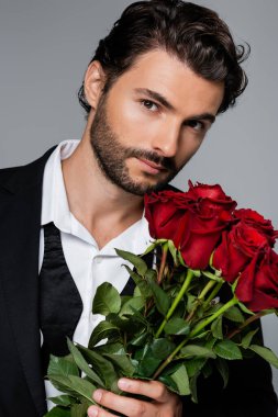 Gri üzerinde kırmızı güller tutan takım elbiseli sakallı adam.