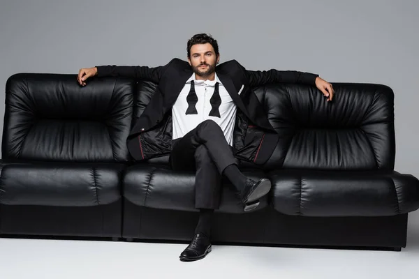 confident man in suit sitting on black leather sofa on grey