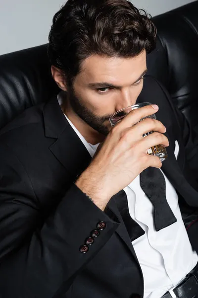 Mężczyzna Formalnym Ubraniu Siedzi Czarnej Sofie Pije Whisky Odizolowaną Szaro — Zdjęcie stockowe