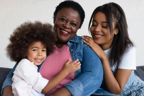 当女儿和孙女在家里拥抱她时 快乐的非洲裔美国老太太对着摄像机笑着 — 图库照片