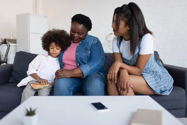 Afrikansk Amerikansk Flicka Tittar Bilderbok Medan Sitter Soffan Med Mormor — Stockfoto