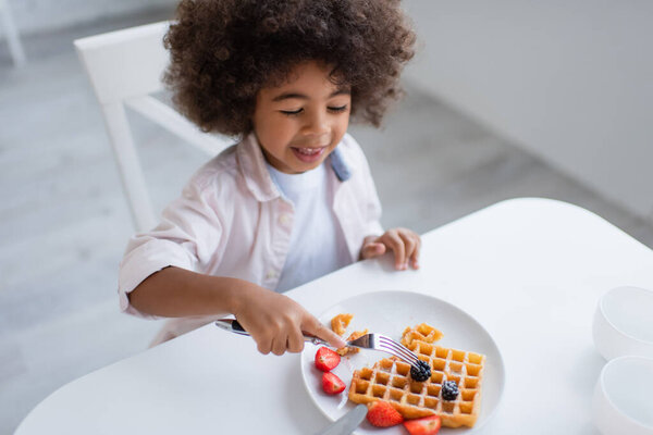 high angle view of african american girl with fork near tasty waffle with fresh berries